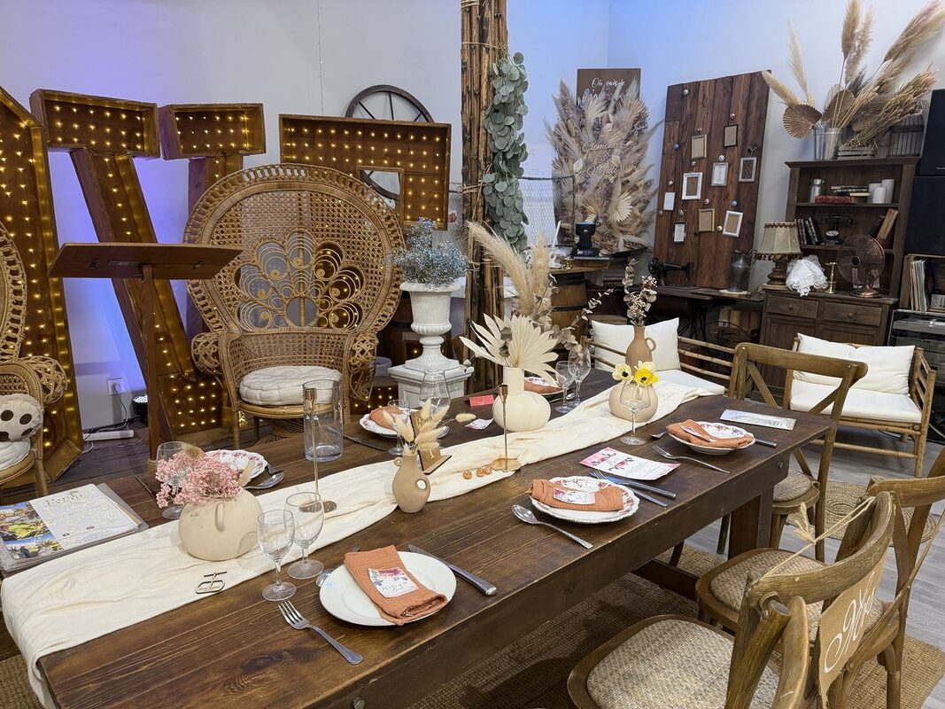 Table bohème dressée au showroom Pink Event : table en bois, chemin de table écru, vases en céramique, fauteuil paon et lettres lumineuses