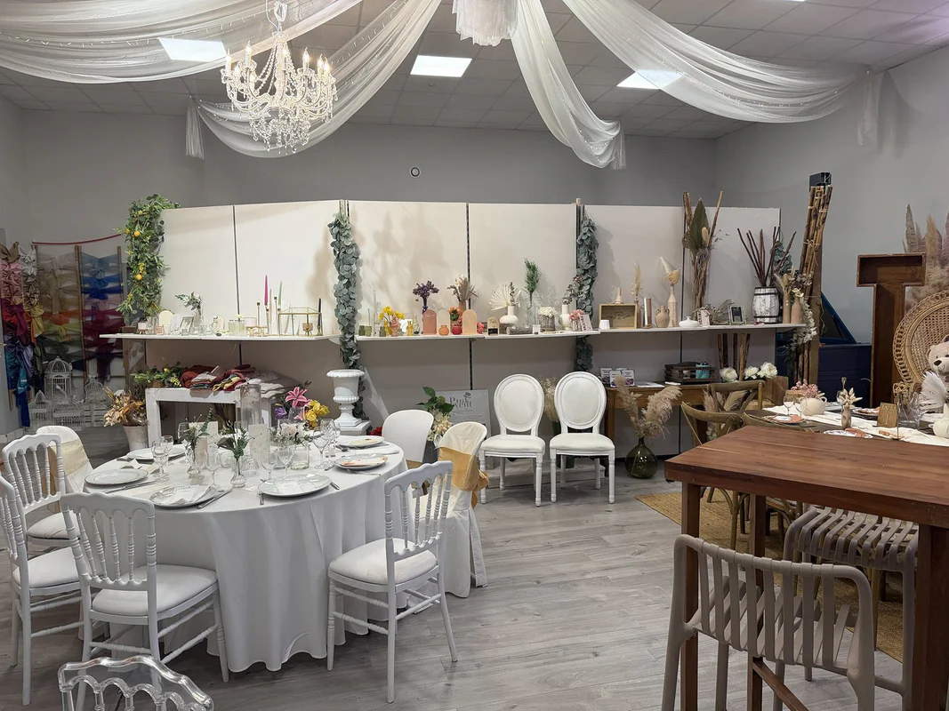 Vue d’ensemble du showroom Pink Event : plafond drapé et lustre en cristal, table ronde dressée, chaises Napoléon blanches et étagères de vases