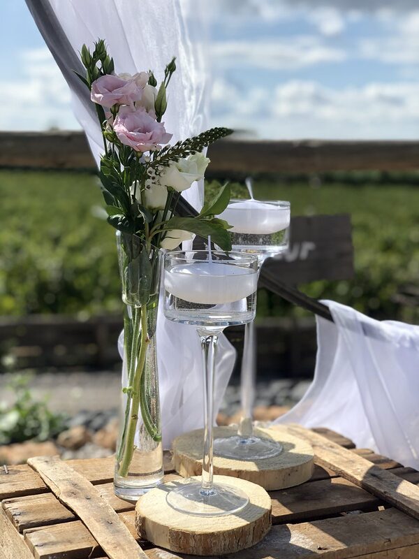 Bougies flottantes sur pied posées sur des rondins de bois et une caisse en bois, soliflore de lisianthus rose, voile blanc de l’arche