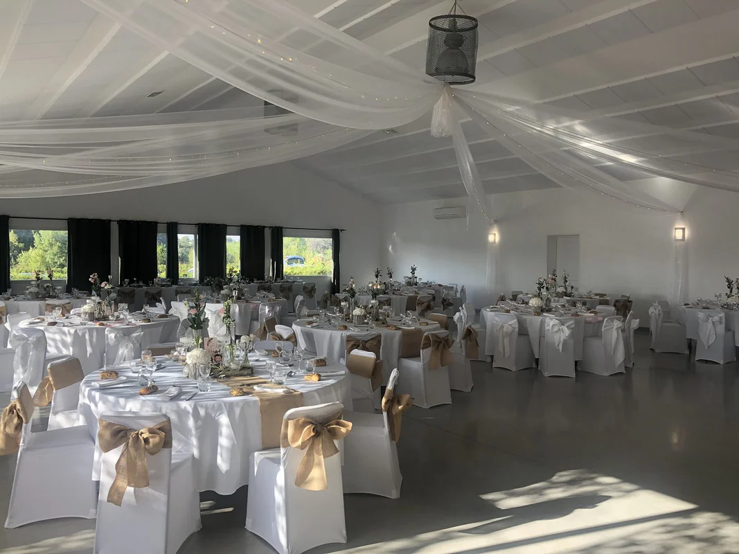 Table d’honneur nappée de blanc : guirlande d’eucalyptus, bougies flottantes sur pied, soliflores et photophores, chaises housées à nœuds de jute