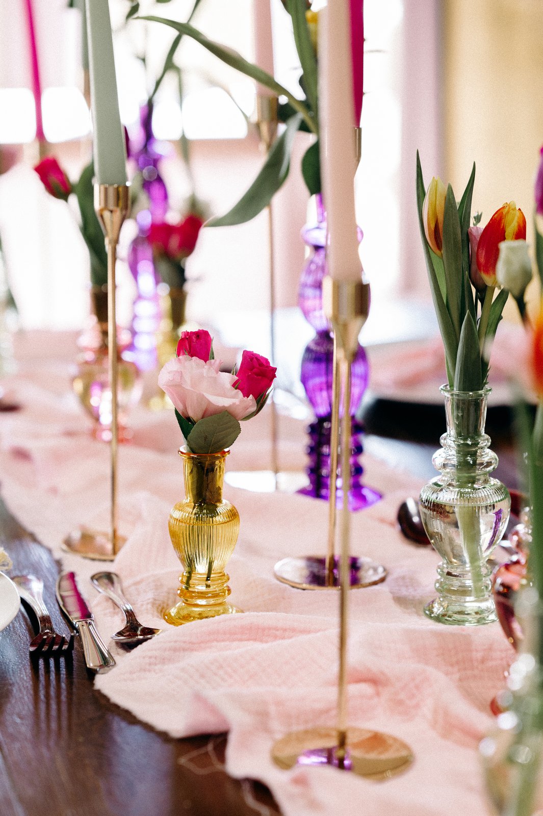 Soliflores en verre ambre, vert et rose garnis de tulipes et de roses, chandeliers dorés sur un chemin de gaze rose