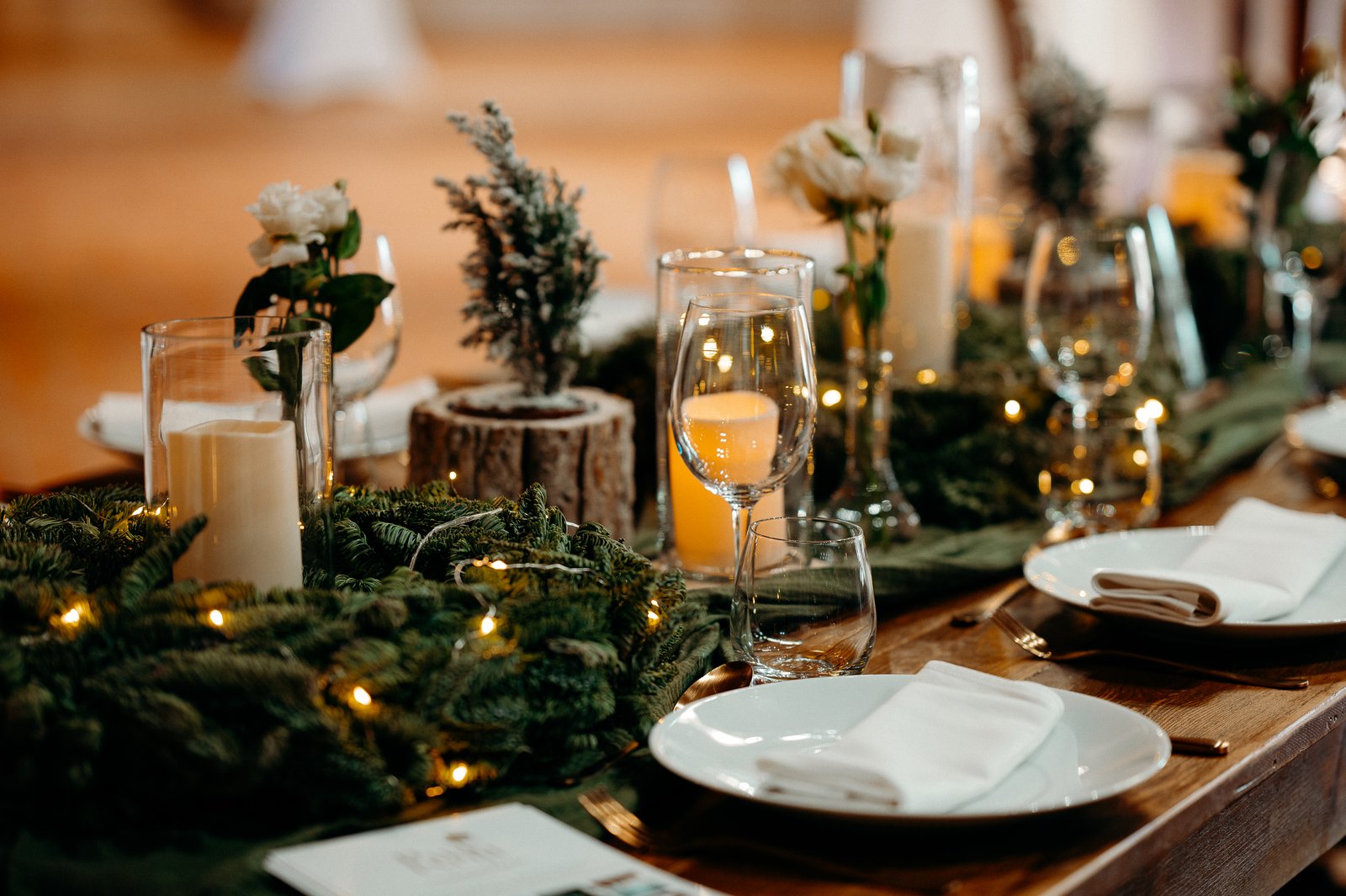 Tablée en bois couverte de branches de sapin et de petites lumières, bougies sous verre, sapins givrés et roses blanches