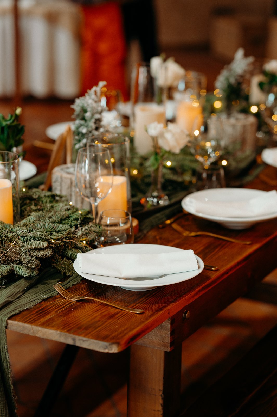 Assiette blanche et serviette pliée sur une table en bois, branches de sapin, guirlande lumineuse et bougies sous verre