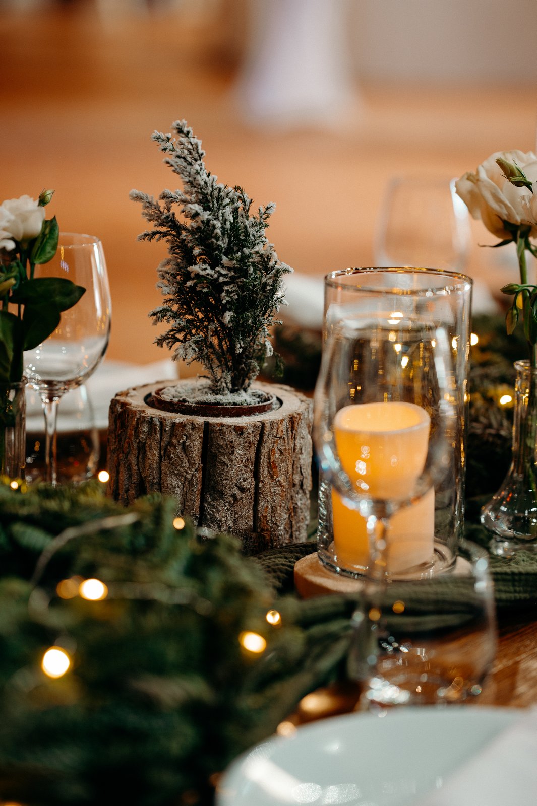 Petit sapin givré dans un rondin d’écorce, bougie dans un cylindre en verre et branches de sapin parsemées de lumières