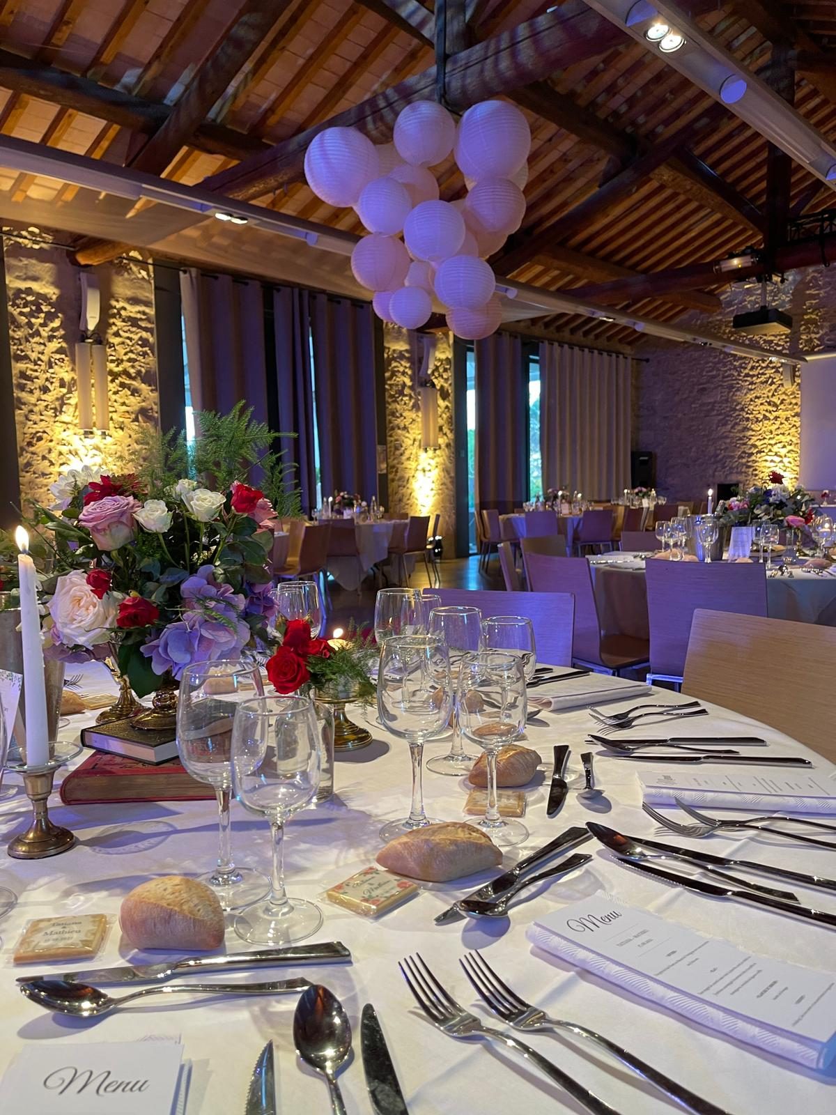 Table ronde dressée avec menus, bougeoir doré et bouquet de roses sur livres anciens, lanternes en papier au plafond