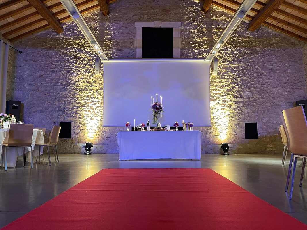 Tapis rouge menant à la table d’honneur au chandelier argenté, mur de pierre éclairé par des projecteurs au sol