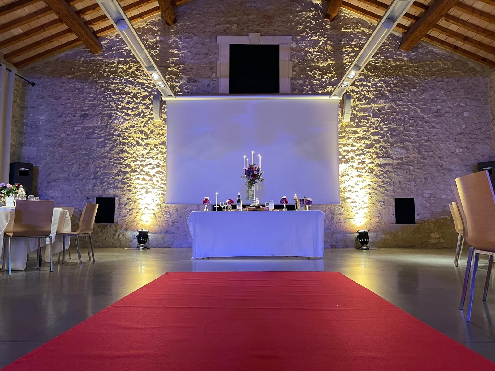 Tapis rouge menant à la table d’honneur au chandelier argenté, mur de pierre éclairé par des projecteurs au sol