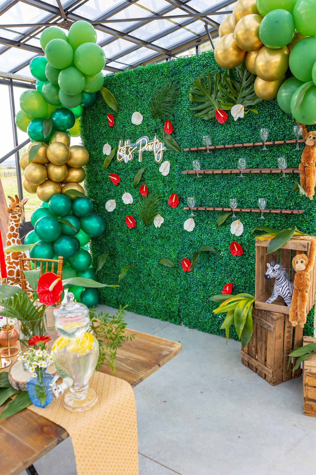 Mur végétal à anthuriums rouges et blancs, étagères à flûtes, caisses en bois avec zèbre et singe en peluche