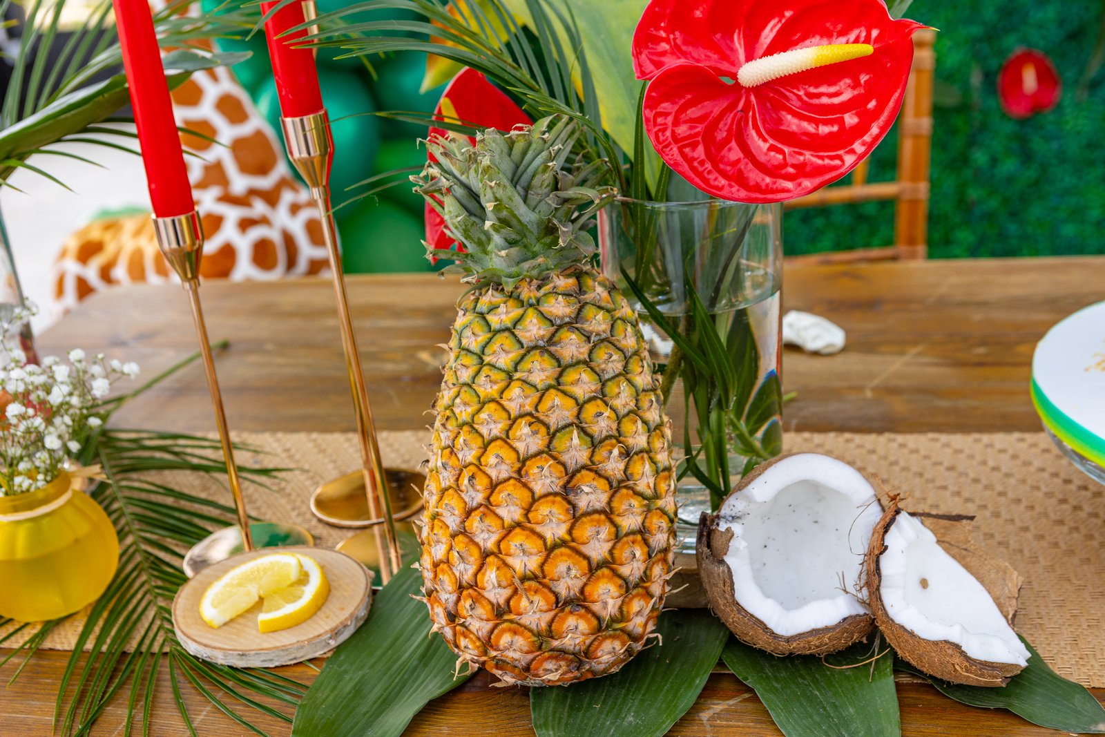 Ananas, noix de coco ouverte, anthurium rouge et bougies rouges sur bougeoirs dorés, sur une table en bois