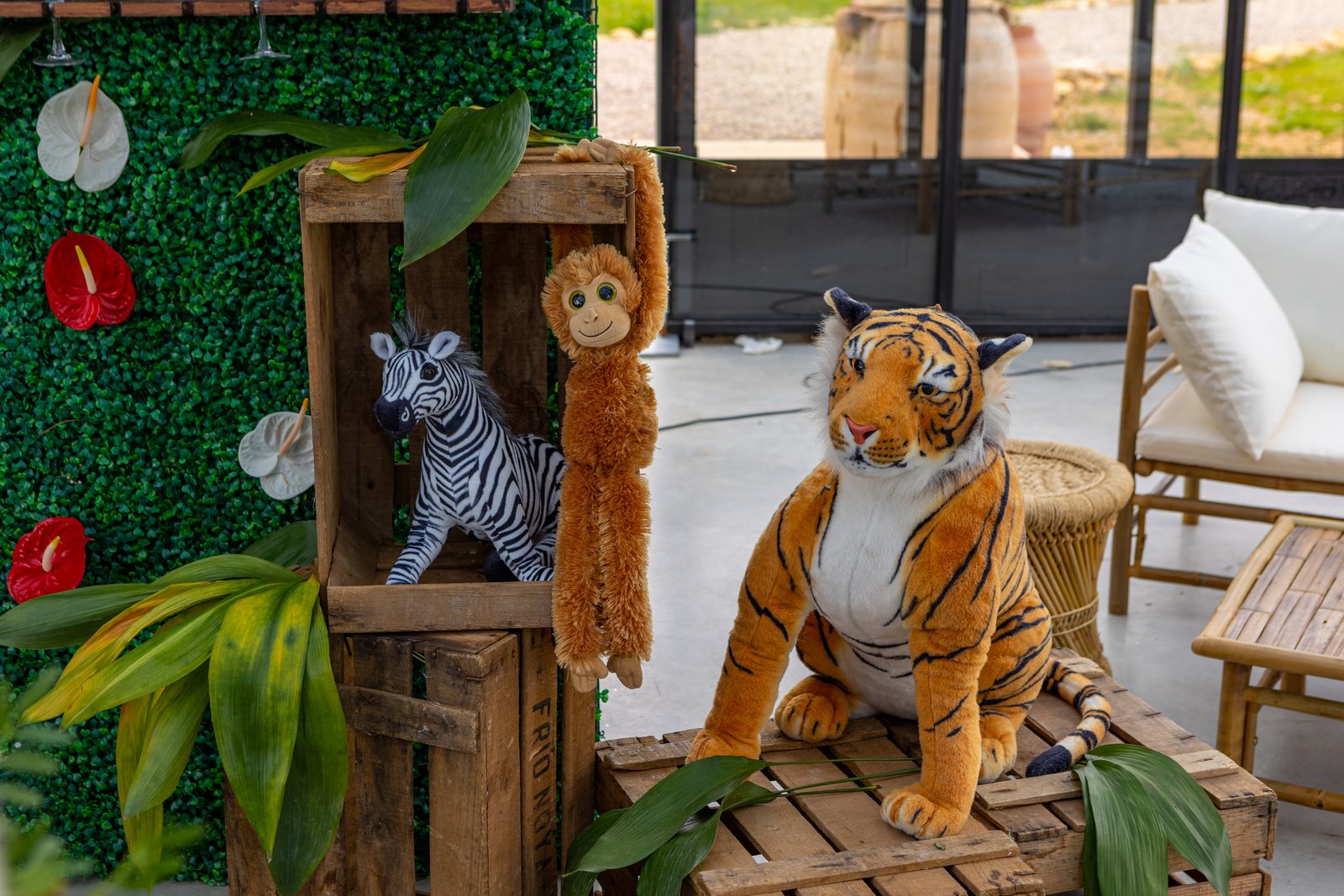 Caisses en bois avec zèbre, singe et tigre en peluche devant un mur végétal, salon en bambou à droite