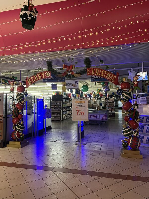 Arche « Merry Christmas » encadrée de piliers de boules géantes à l’entrée d’un magasin, guirlandes lumineuses au plafond