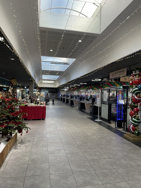 Allée de la galerie sous des guirlandes lumineuses, sapin décoré, pilier de boules géantes et arche de ballons aux caisses