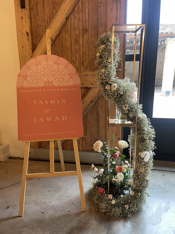 Panneau de bienvenue sur chevalet en bois et cascade de gypsophile, roses et lisianthus sur une structure dorée à l’entrée de la salle
